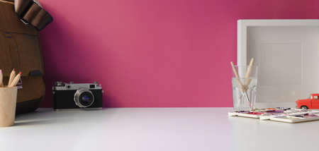 Stylish workspace with copy space, camera and office supplies on white table and pink wall backgroundの写真素材