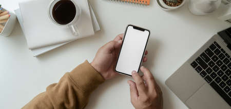 Top view of young male freelancer holding blank screen smartphone in his modern workplace の写真素材