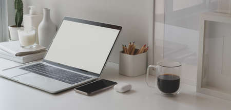 Minimal workspace with open blank screen laptop computer and office supplies on white wooden tableの写真素材