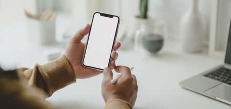 Cropped shot of young male freelancer holding blank screen smartphone in his modern workplace 