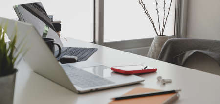 Cropped shot of comfortable workspace with laptop computer and office supplies on white table next...