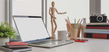 Cropped shot of comfortable workspace with laptop computer and office supplies on white table next to the windowsの写真素材