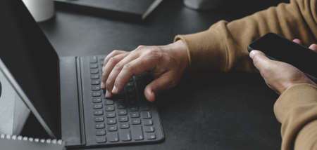 Cropped shot view of young man typing on keyboard while working on his project in dark modern workplaceの写真素材