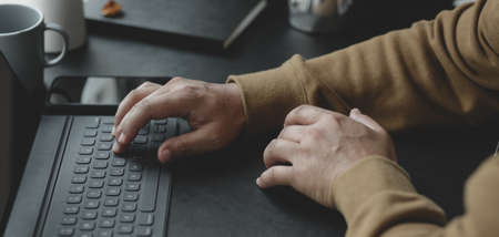 Close-up view of young man typing on keyboard while working on his project in dark modern workplaceの写真素材