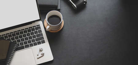 Close-up view of dark trendy workspace with laptop computer, coffee cup and office supplies with copy space の写真素材