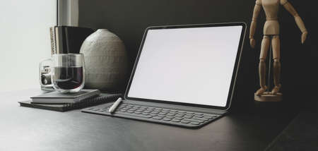 Cropped shot of modern workplace with blank screen tablet with office supplies with black wall backgroundの写真素材