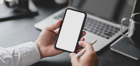 Cropped shot of professional businessman holding blank screen smartphone in dark modern office roomの写真素材