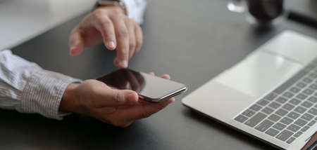 Cropped shot of young professional businessman using smartphone in his modern office roomの写真素材