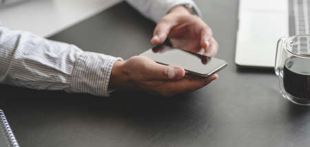 Close-up view of young professional businessman using smartphone while working on his projectの写真素材