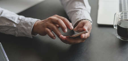 Cropped shot of young professional businessman using smartphone in his modern office roomの写真素材