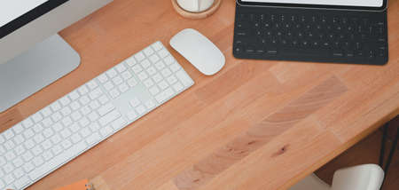 Cropped shot of comfortable workplace with keyboard computer and desktop computer with other office supplies on wooden table の写真素材