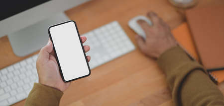 Close-up view of man holding blank screen smartphone while working on his project in his cozy...