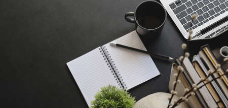 Overhead shot of dark modern workplace with laptop computer and office supplies on black table backgroundの写真素材