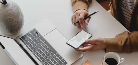 Close-up view of male freelancer working on his project with blank screen smartphone in his comfortable offie roomの写真素材