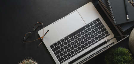 Top view of dark modern workplace with laptop computer and office supplies on black table background