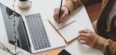 Cropped shot of male freelancer working on his project while writing his ideas on notebook in comfortable workspaceの写真素材