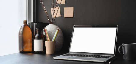 Dark trendy office room with blank screen laptop computer and office supplies with decorationsの写真素材