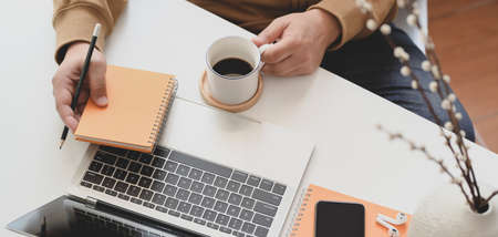 Cropped shot of young man working in his comfortable workplace while drinking a cup of coffeeの写真素材
