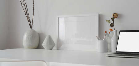 Minimal office room with mock up frame and open blank screen laptop computer on white tableの写真素材