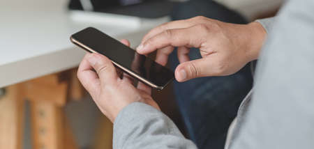 Close-up view of businessman holding his smartphone in relax sitting movement in his office roomの写真素材