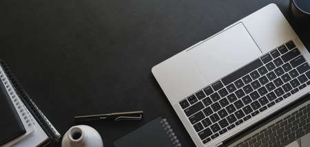 Overhead shot of trendy office room with laptop computer and office supplies with copy space on black table backgroundの写真素材
