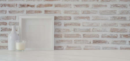 Minimal workspace with mock up frame and office supplies on white table with copy space and brick wall backgroundの写真素材
