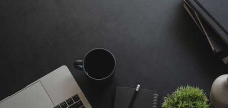 Overhead shot of dark modern workplace with laptop computer and office supplies on black table backgroundの写真素材