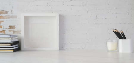Minimal workspace with mock up frame and office supplies on white table with copy space and brick wall backgroundの写真素材