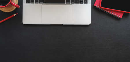 Top view of modern workplace with laptop computer and red office supplies on black table background
