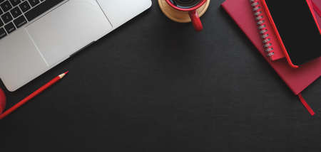 Top view of modern workplace with laptop computer and red office supplies on black table background
