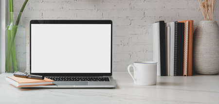 Cropped shot of blank screen laptop computer with books and office supplies with coffee cup in...