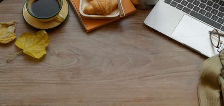 Top view of comfortable workplace with laptop computer and office supplies with breakfast on wooden table and copy spaceの写真素材
