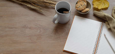 Top view of comfortable autumn workspace with open notebook and coffee cup with office supplies on wooden tableの写真素材