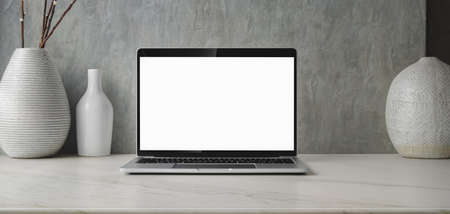Minimal workspace with blank screen laptop computer and ceramic vase decorations with copy spaceの写真素材