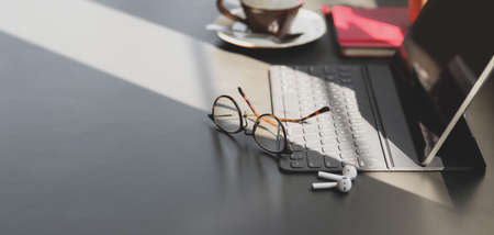 Modern office room with digital tablet and office supplies on dark grey table with copy space and sunlightの写真素材