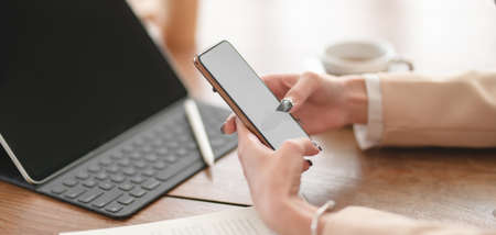 Close-up view of young businesswoman using her smartphone while working on her project in comfortable workspaceの写真素材