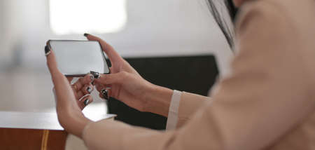 Cropped shot of young businesswoman using mock-up smartphone while working on her project in comfortable office roomの写真素材