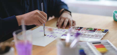 Cropped shot of young artist painting on sketch paper with water colour in comfortable workplace