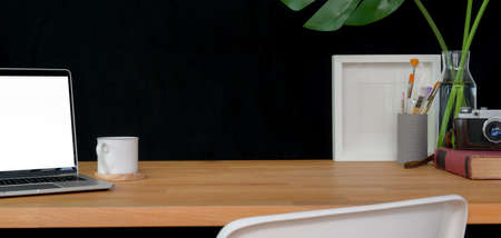 Cropped shot of trendy workspace with laptop computer, office supplies and copy space on wooden table and black backgroundの写真素材