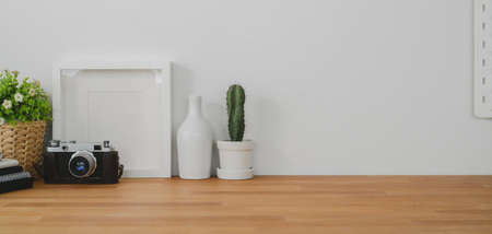 Cropped shot of comfortable office room with mock up frame, decorations and copy space on wooden table and white wall backgroundの写真素材