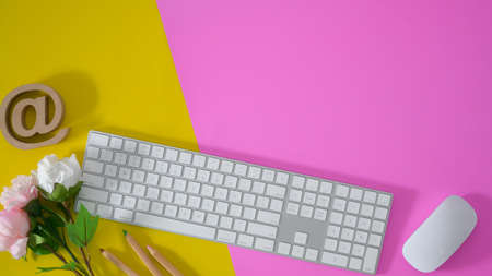 Top view of colourful workspace with keyboard and office supplies on yellow and pink desk background...