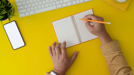 Top view of young man working on his project by writing on notebook in trendy workplace