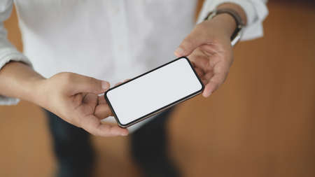 Cropped shot of man holding mock-up smartphone while standing in comfortable office room