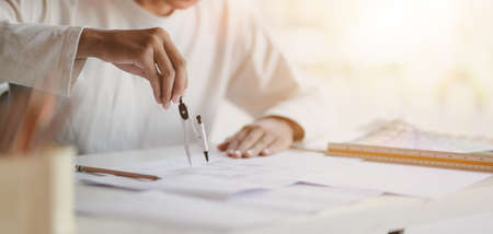 Close-up view of young professional architect working on working on construction plans in modern...