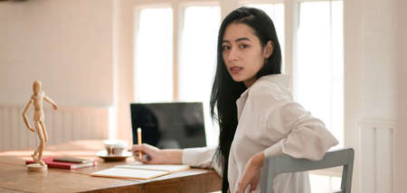 Portrait of young beautiful businesswoman working on her project while looking at the camera in comfortable roomの写真素材