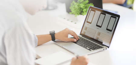 Cropped shot of young passionate UX web development working on his smartphone template with laptop...