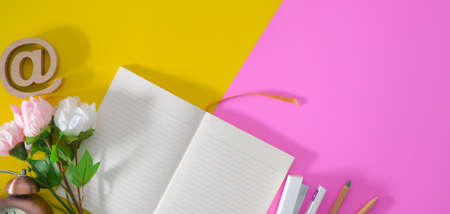 Top view of colourful workplace with open notebook and decorations on pink and yellow desk background の写真素材