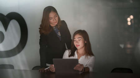 Portrait of young hard-working asian businesswoman working late night on their project while using tablet in modern office roomの写真素材