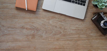 Overhead shot of comfortable workplace with laptop computer, camera and office supplies on wooden table backgroundの写真素材