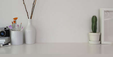 Cropped shot of minimal workplace with paint tools and office supplies on white table and white wall background の写真素材